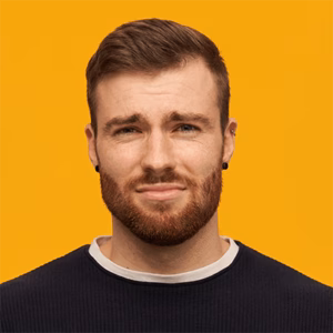 bearded begging man with brunette hair looks regretful has piercing wearing black sweater holds palms together plead something isolated yellow wall